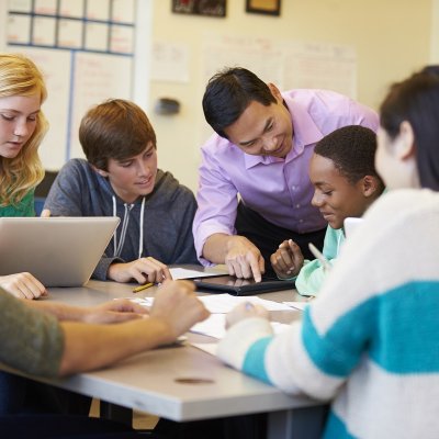 Teacher talking to a group of students at a table.