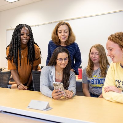 Students and professor looking at a cell phone screen,