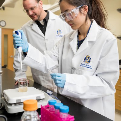 Joshua Reineke, associate professor in the Department of Pharmaceutical Sciences, assists a student working in a lab on campus.