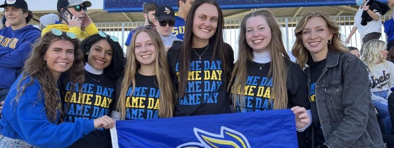 Six members of the university program council holding a Jackrabbits flag.