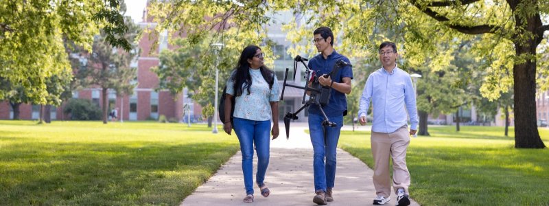 students and faculty walking on campus holding a drone.