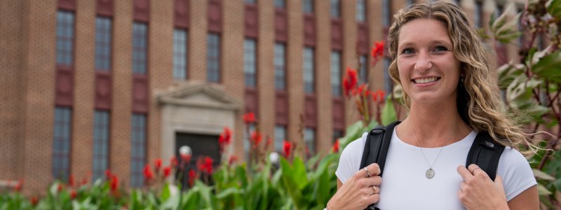 A student standing in front of a flower bed boasting red flowers in front of Lincoln Hall