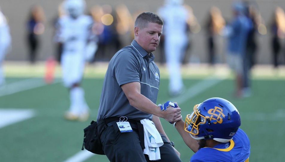 Athletic trainer helping football player up from the field.