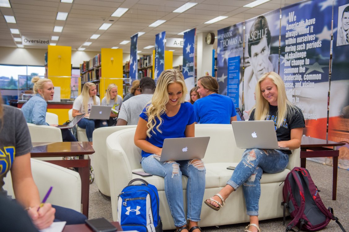 Students sitting in groups and studying on laptops at the library.