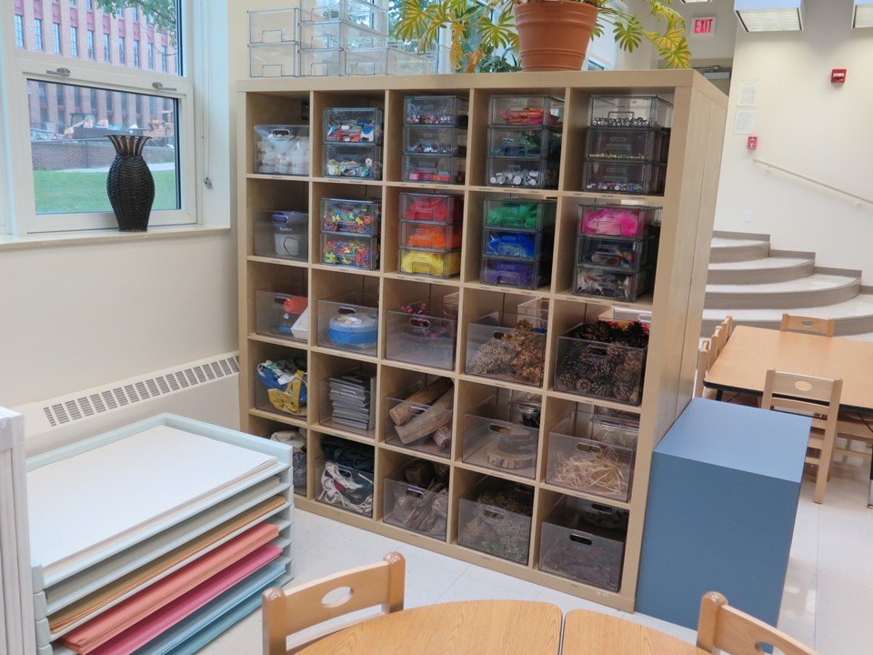 A shelving unit full of a variety of collaging type materials such as colored feathers, sequins, jewels and natural materials.