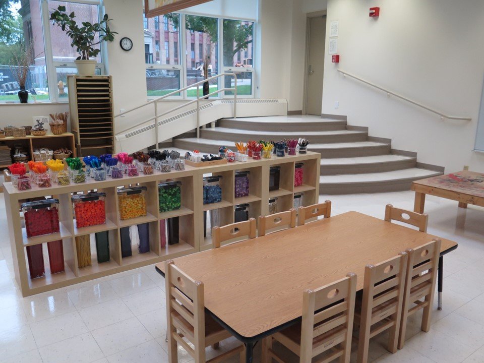 Another perspective from the art studio showing a table, a shelf with pipe cleaners, markers, pom poms and the windows to the outside.