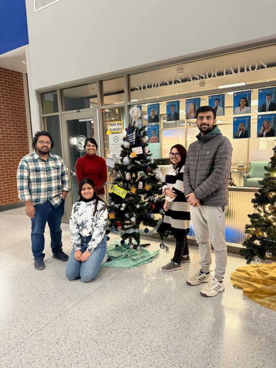 Four graduate student and their advisor standing near a decorated Christmas tree in the student union.