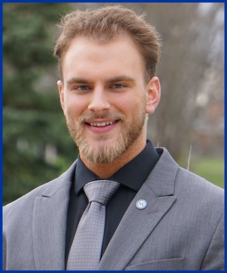 Student's Association College of Natural Sciences senator Matthew Schell sitting on a bench outside smiling
